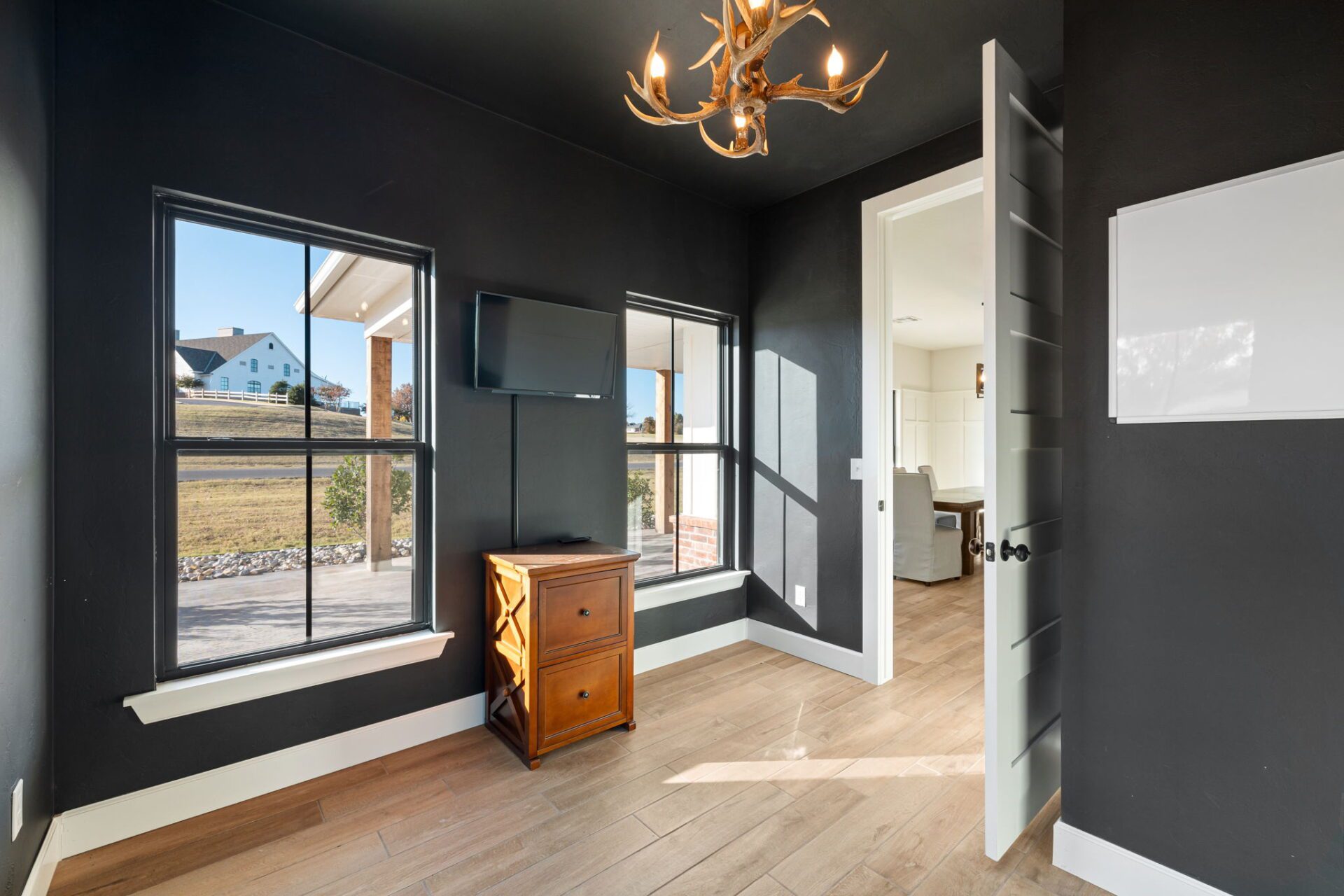 Modern room with dark walls, antler chandelier, wooden floor, mounted TV, and window view.